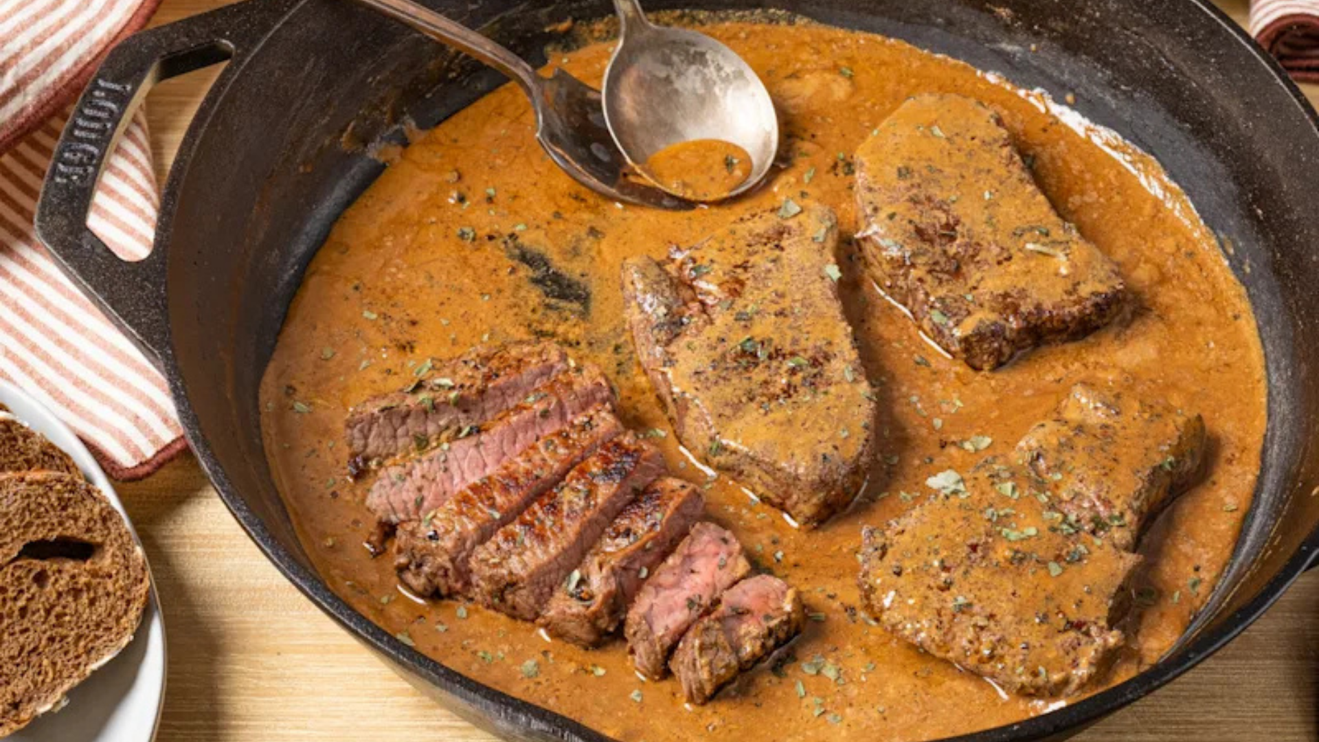 Slices of cast iron-seared Hoosier ribeye steak served in a skillet with a rich bourbon glaze sauce.