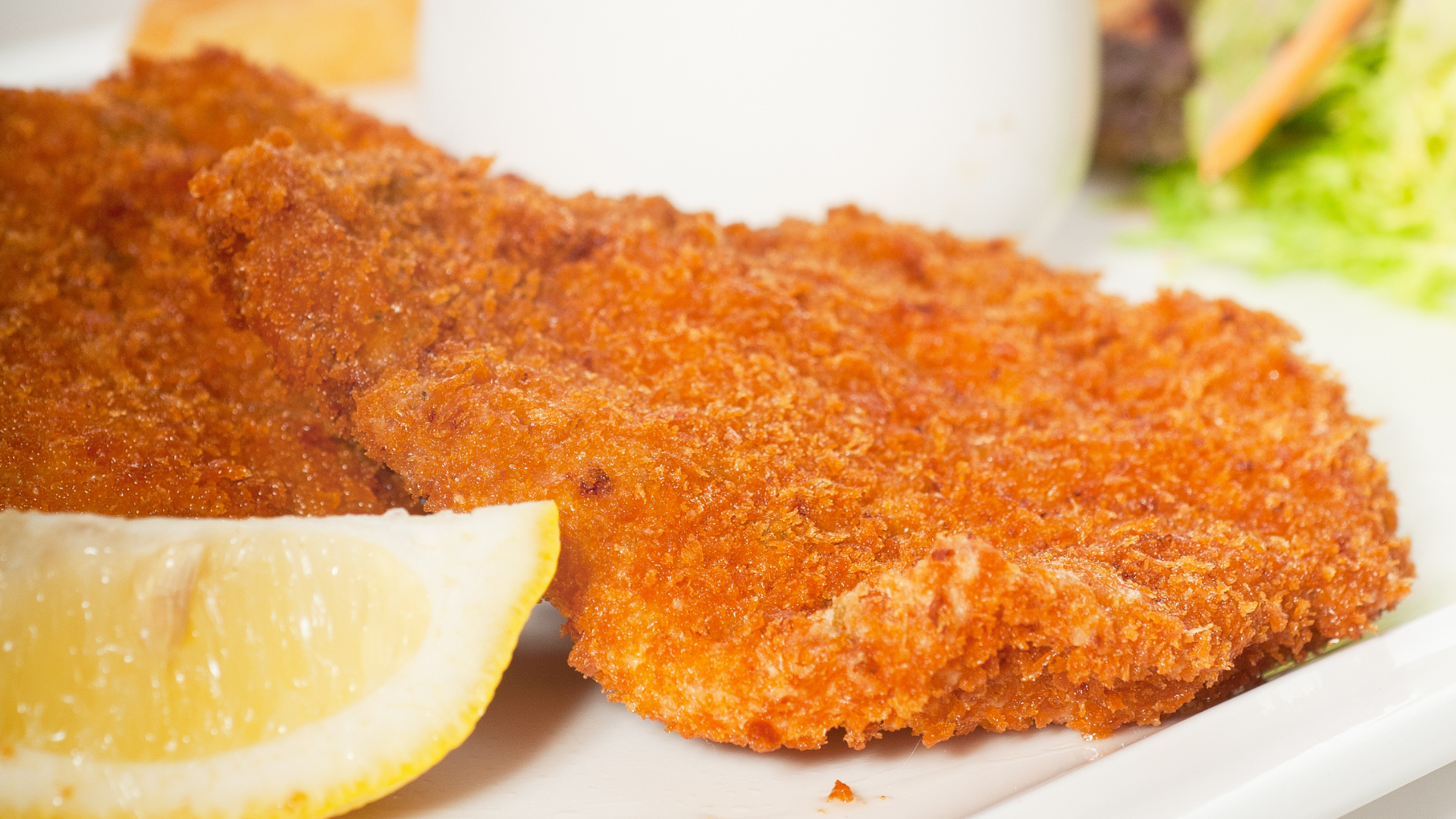 Golden, breaded veal cutlets served with a lemon wedge and a light side salad in the background.