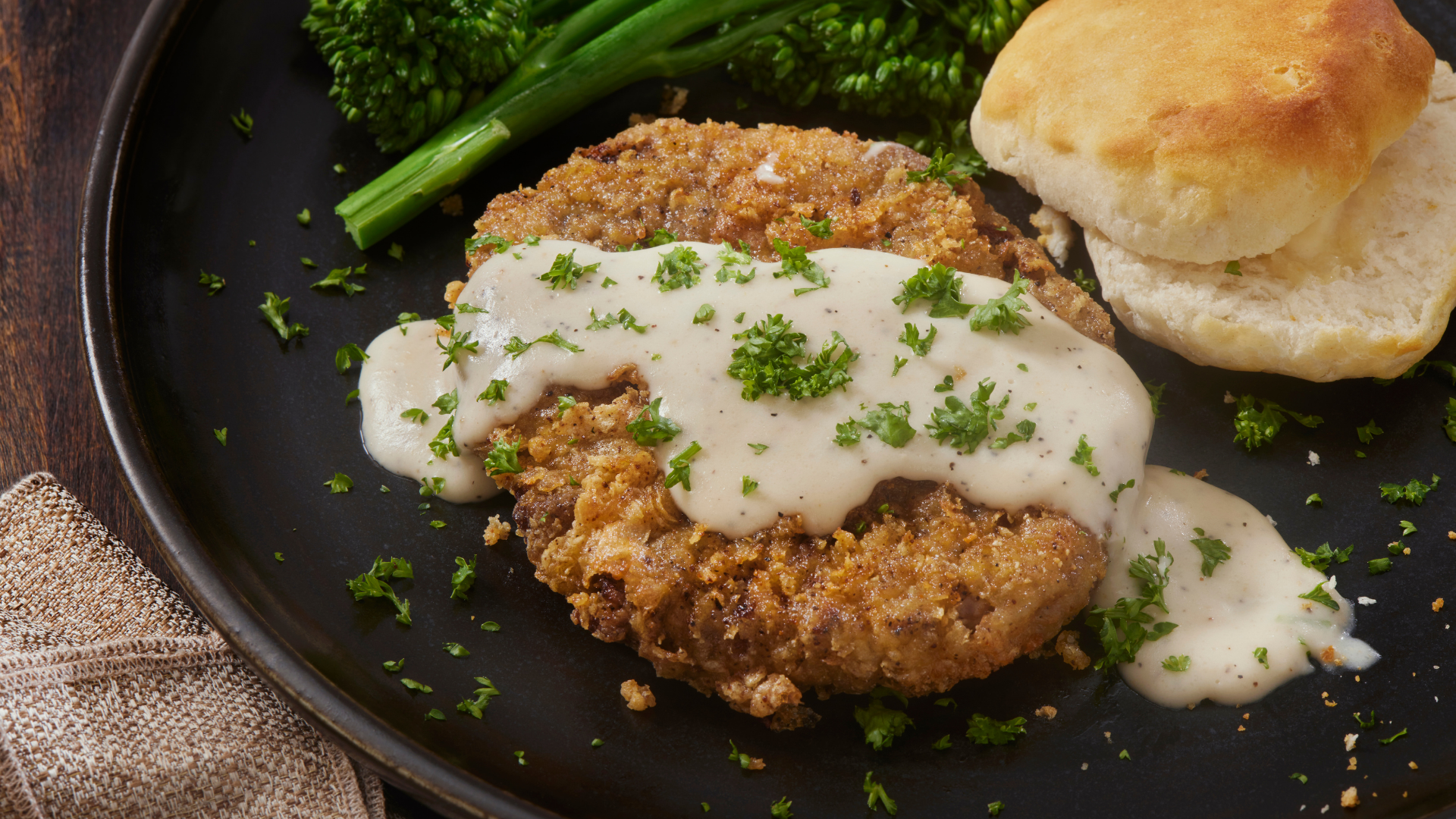 Country-style breaded cube steak smothered in creamy gravy, served with a biscuit and broccolini.