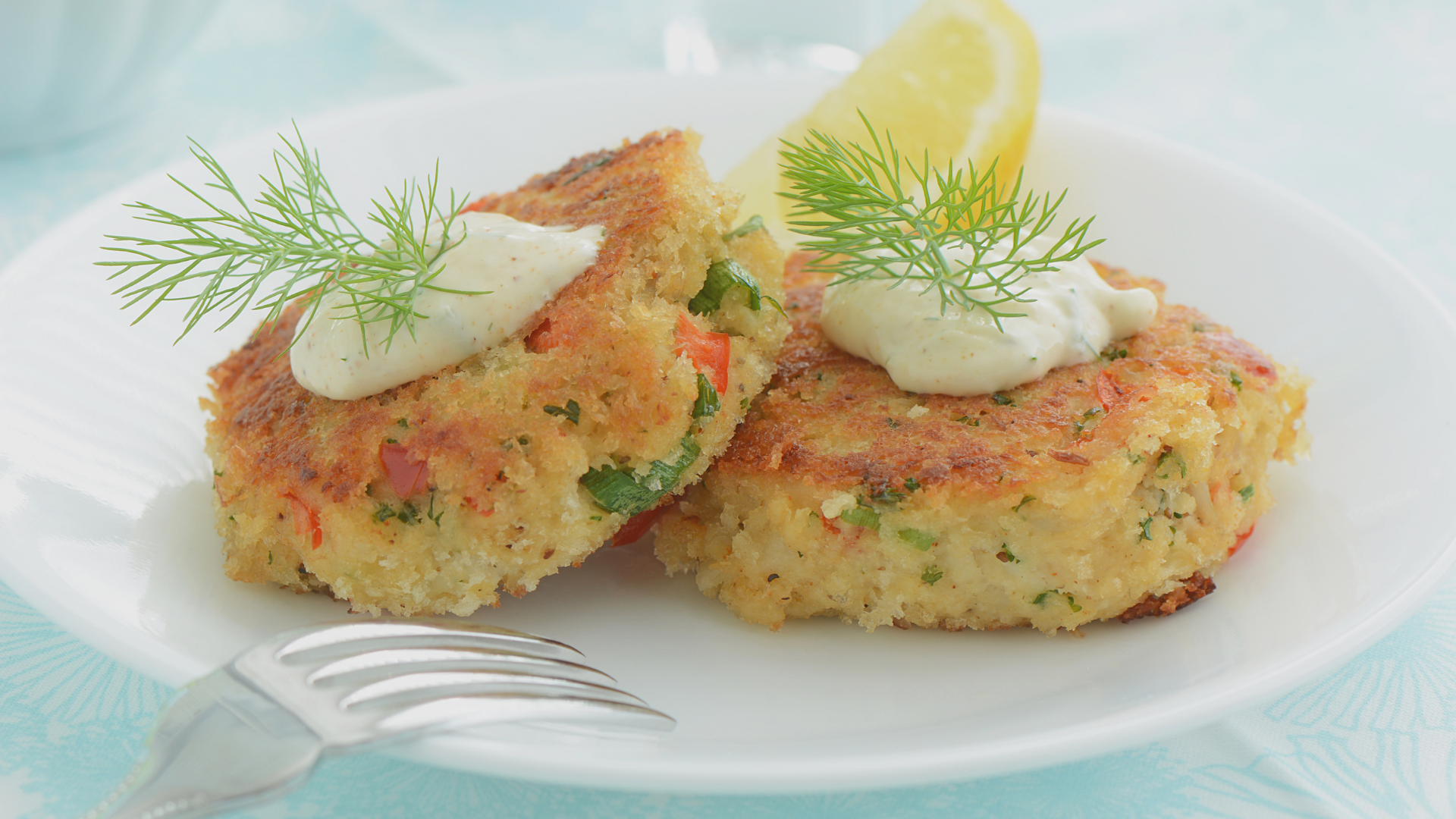 Golden-brown crab cakes topped with creamy lemon-dill sauce and garnished with fresh dill, served with a lemon wedge.