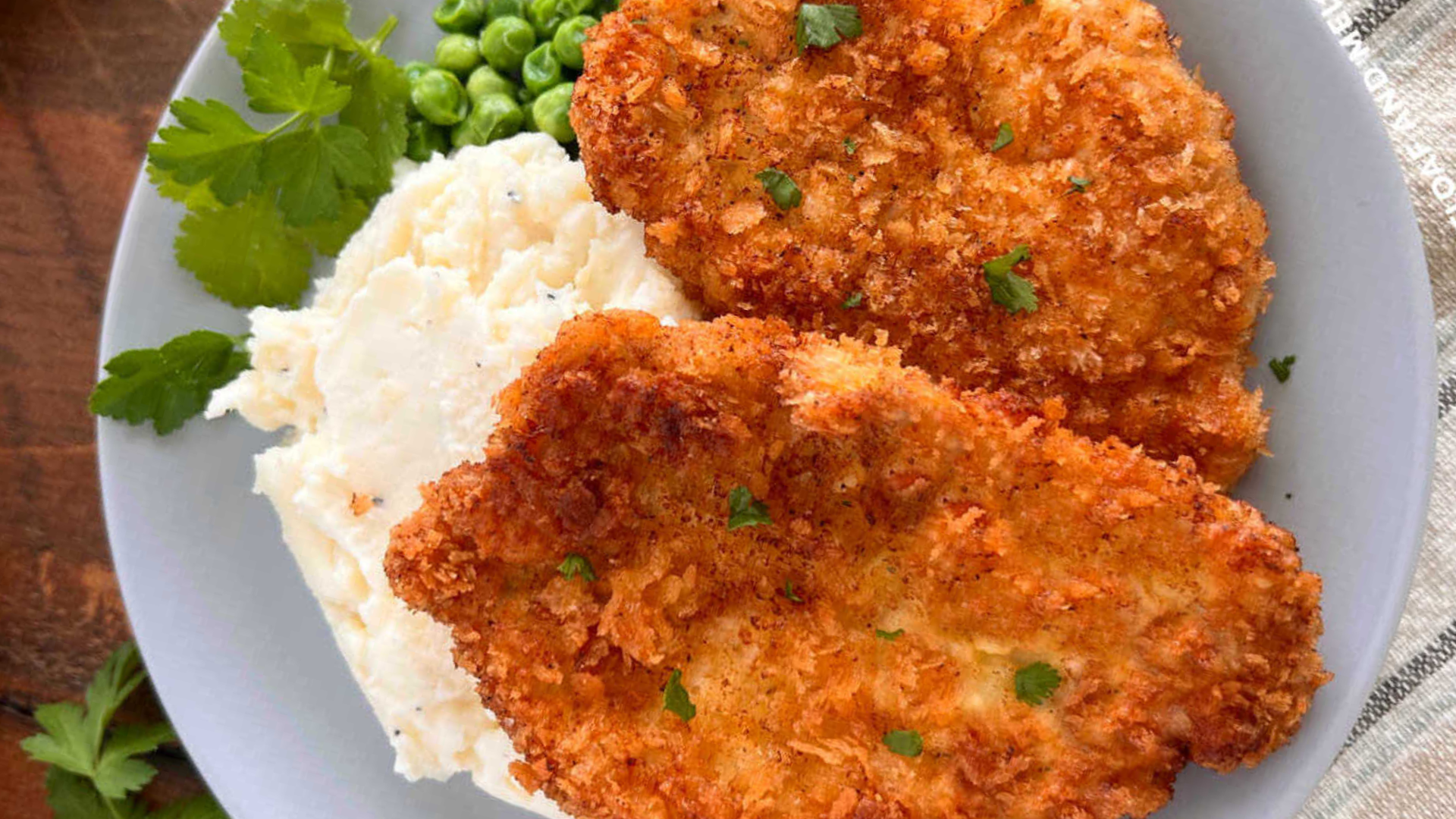 Golden-brown crispy pork cutlets served with creamy garlic mashed potatoes and green peas on a white plate.