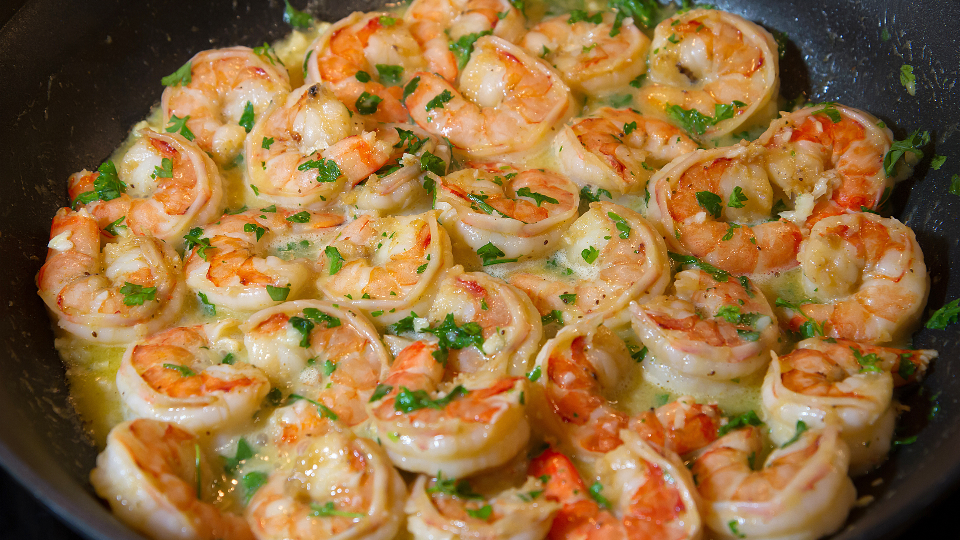Juicy Argentinian red shrimp sautéed in a garlic butter sauce, garnished with fresh herbs in a black skillet.