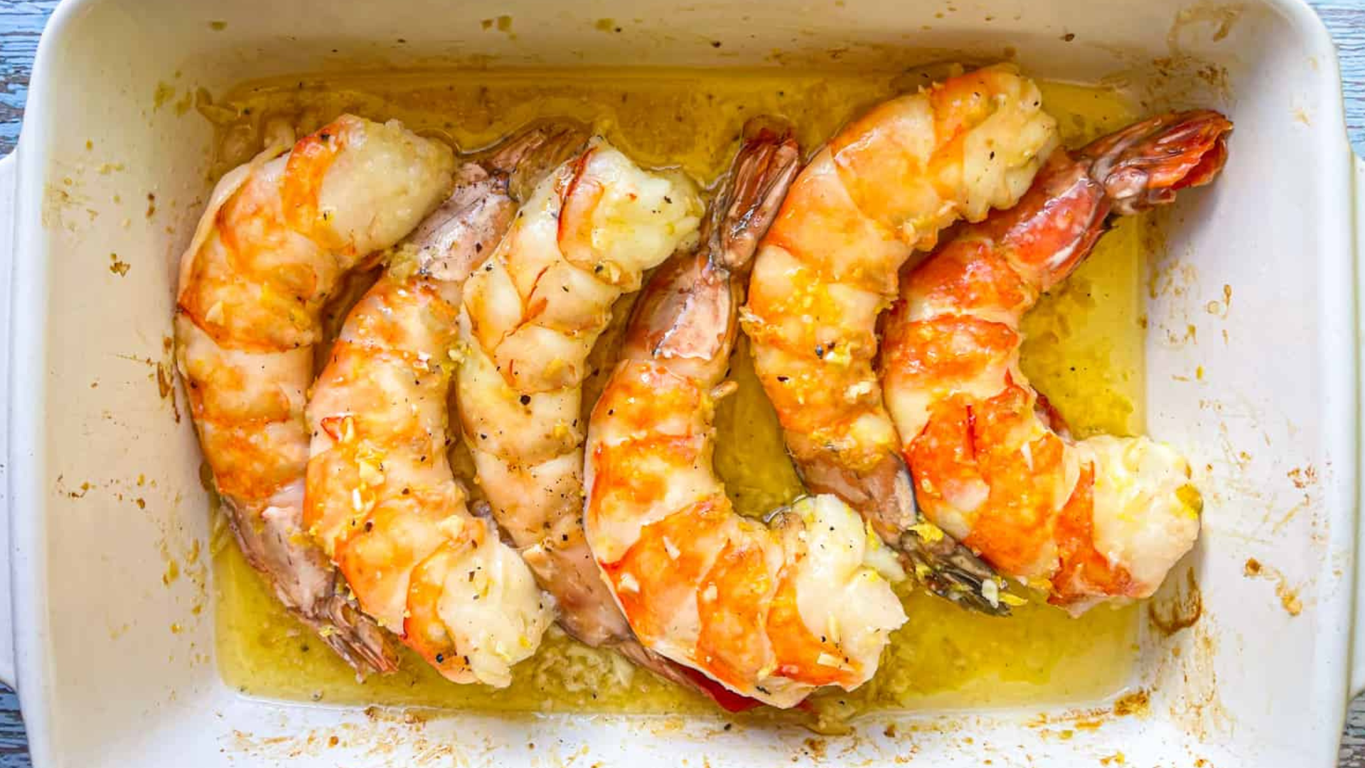 Colossal cooked shrimp baked in a garlic lemon butter sauce, served in a white dish with a golden glaze.