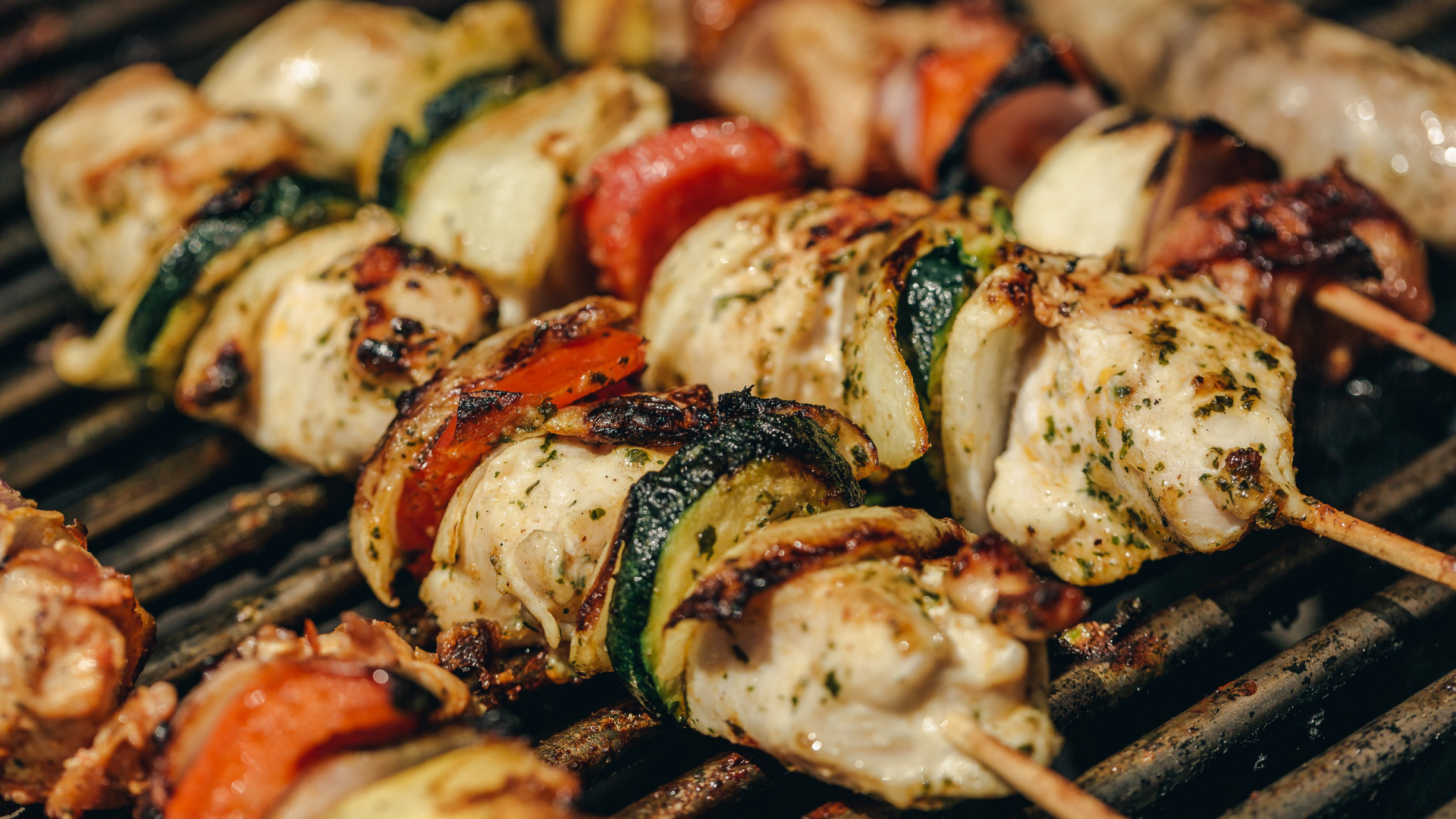 Colorful grilled chicken kabobs with zucchini, onion, and red pepper on a barbecue grill.