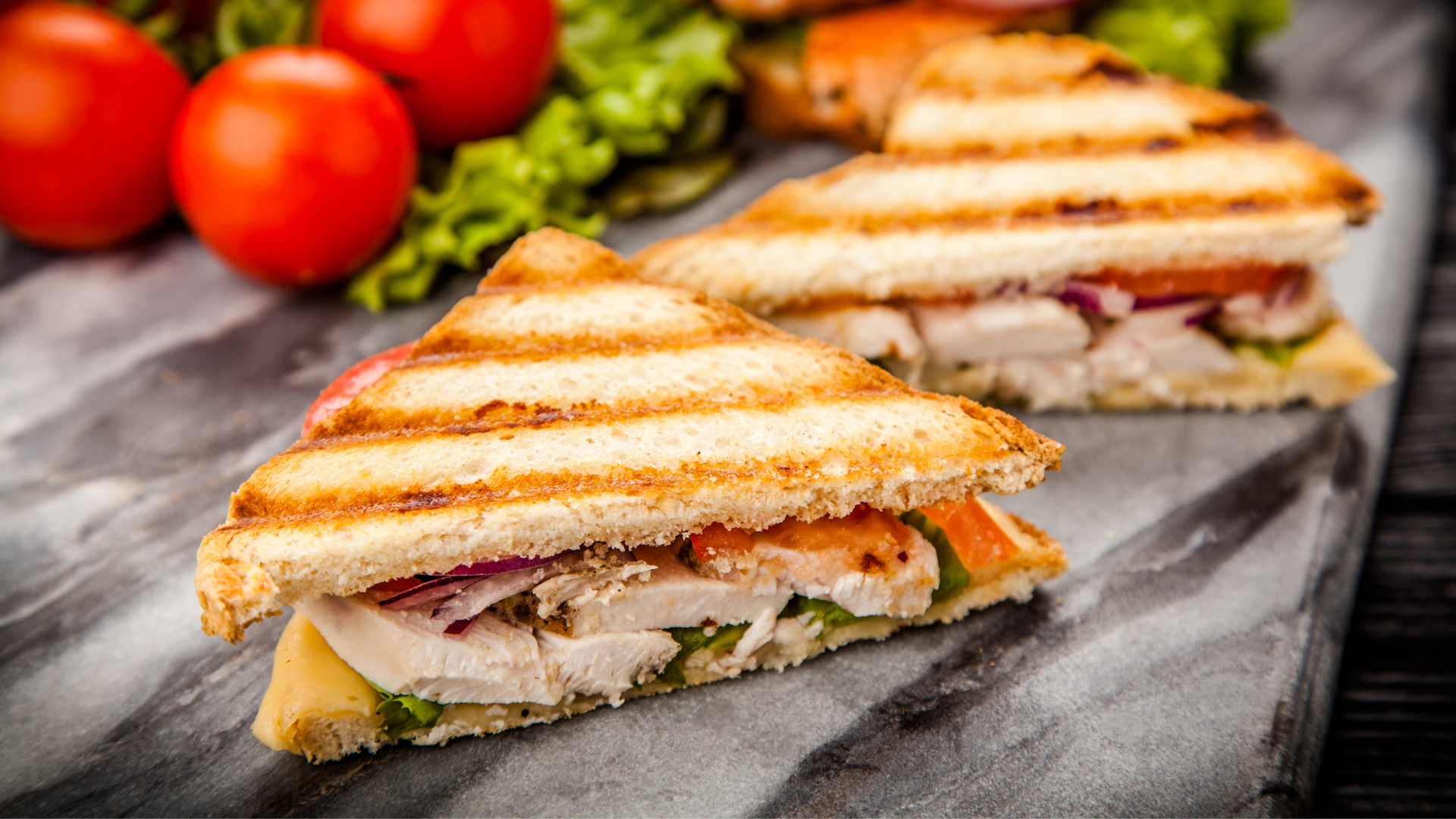 Grilled chicken sandwich made with sliced Amish chicken breast, fresh tomatoes, red onion, lettuce, and cheese, served on toasted sandwich bread.