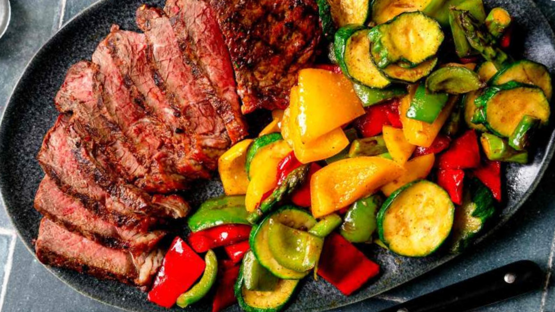 Sliced marinated vacio steak served with colorful grilled vegetables including bell peppers, zucchini, and asparagus.