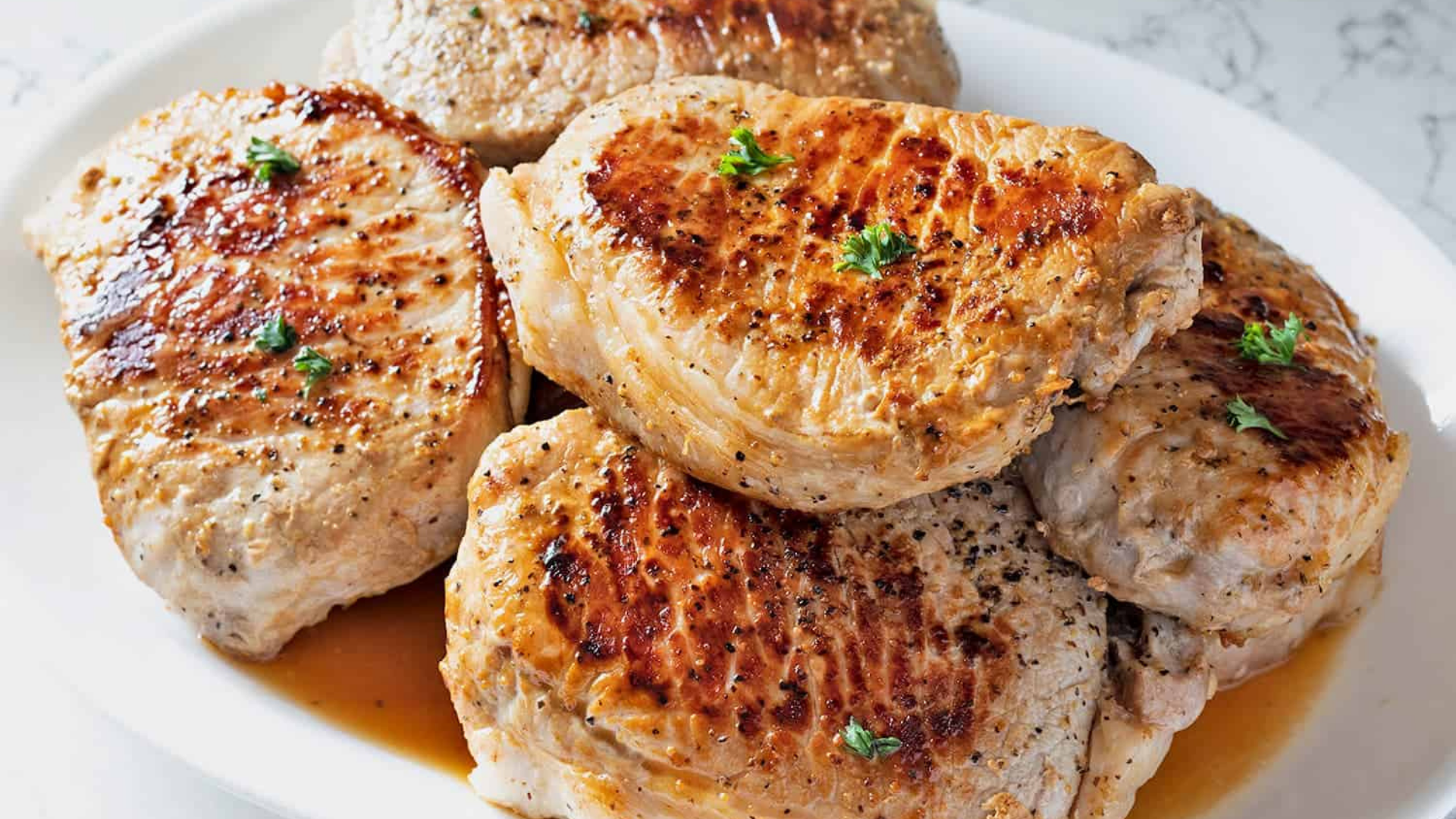 Juicy, golden-brown pan-seared boneless pork chops on a white serving platter, lightly garnished with parsley.