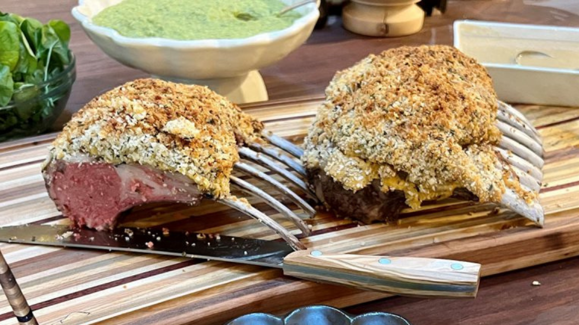 Rack of lamb rib chops coated in a golden Dijon mustard and herb crust, sliced and served on a wooden board with dipping sauces.