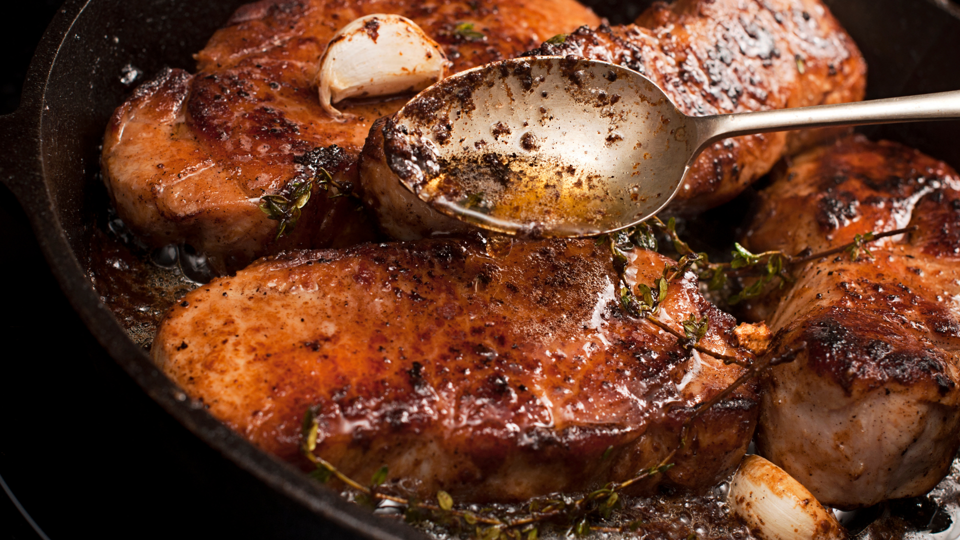 Pork loin chops seared in a cast iron skillet, basted with apple cider glaze and garnished with garlic and thyme.