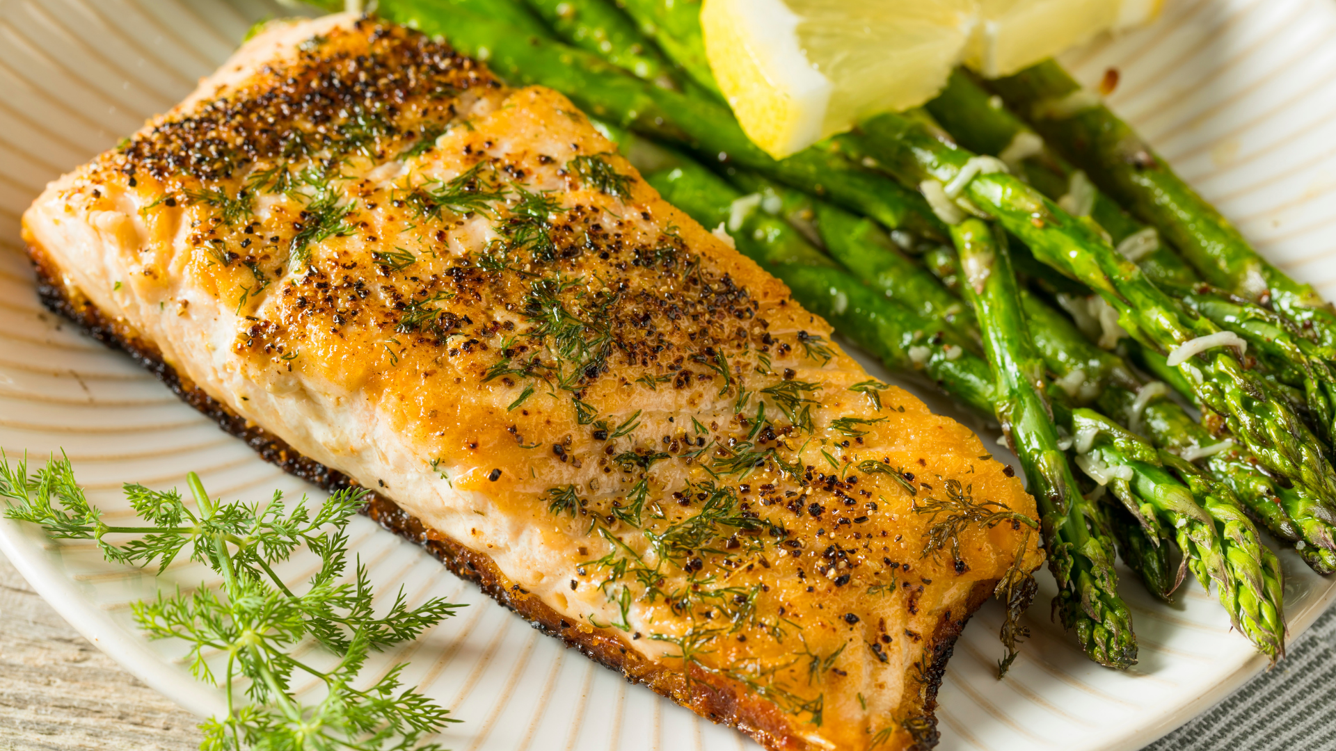 Pan-seared sockeye salmon fillet topped with garlic herb butter and served with roasted asparagus and a lemon wedge.