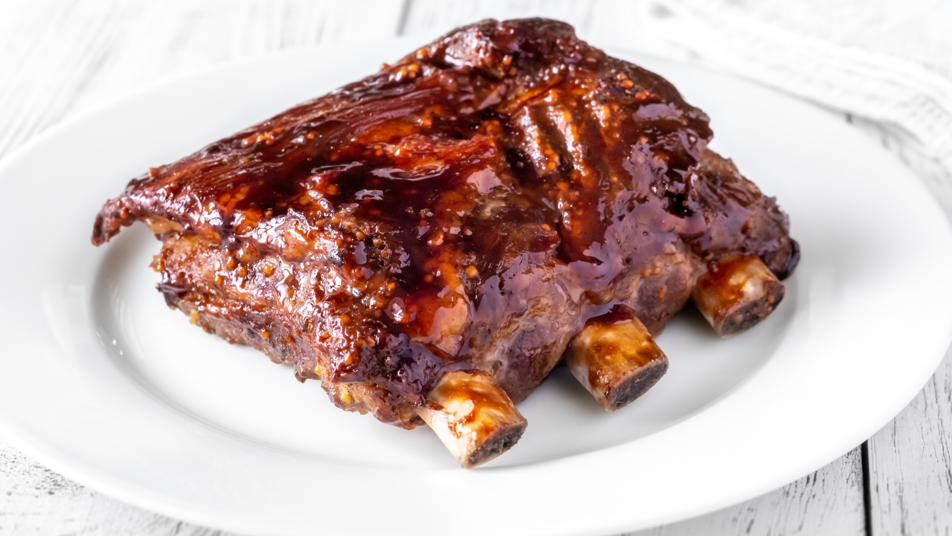 A plate of slow-roasted country-style pork ribs coated in a thick, glossy barbecue glaze, served on a white dish.