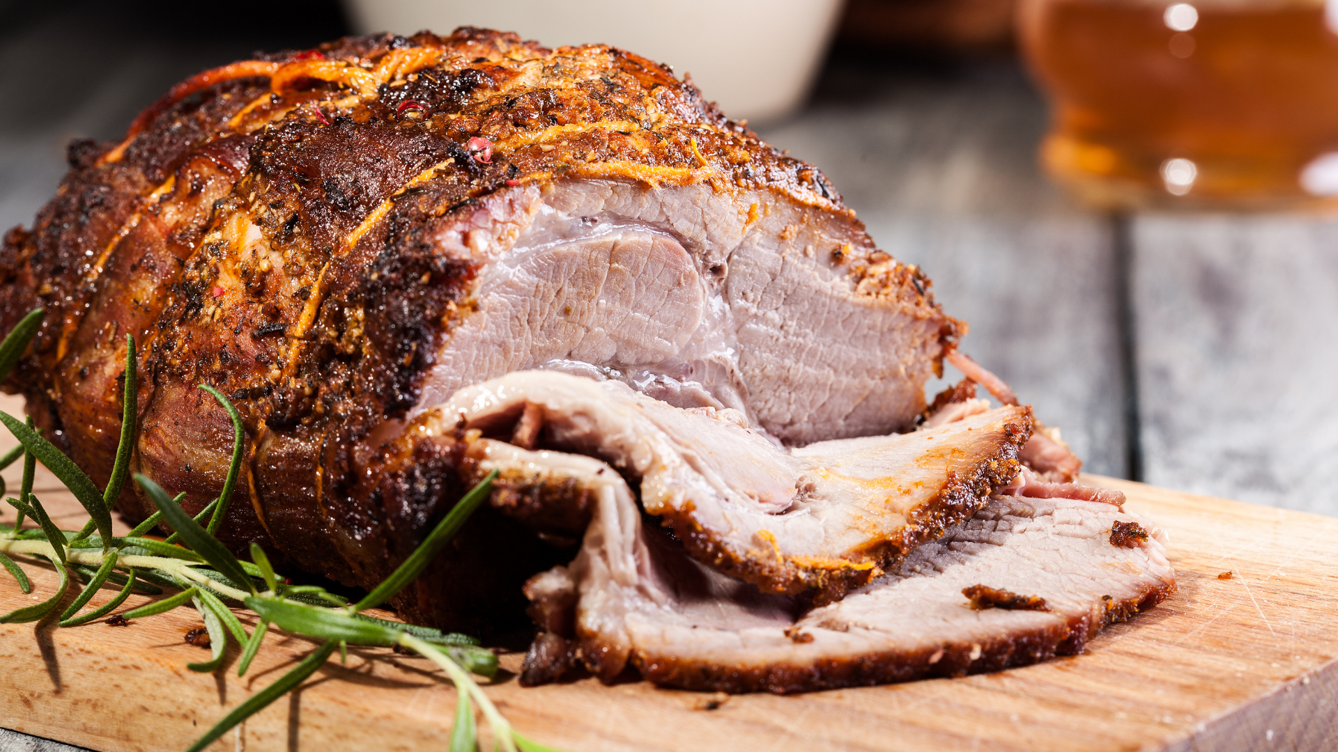 Juicy, slow-roasted pork shoulder with a crispy herb crust, sliced and served on a wooden cutting board with a sprig of rosemary.