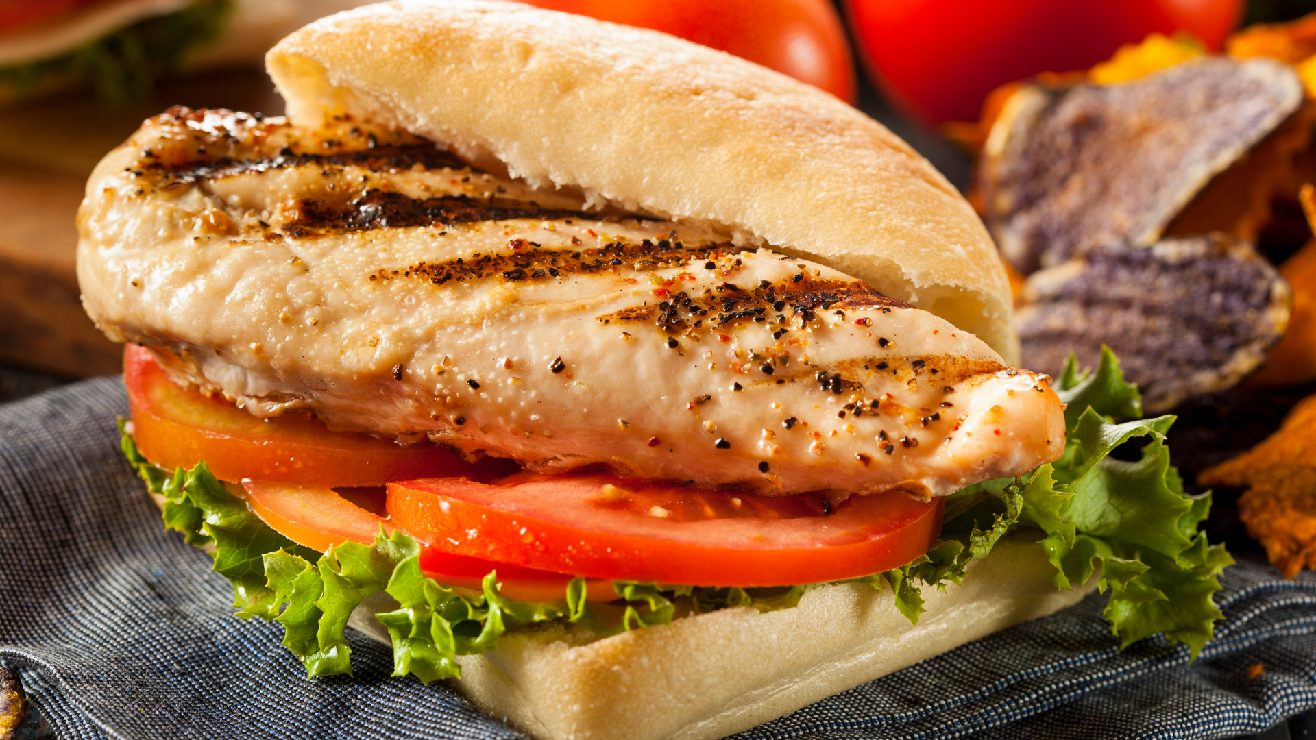 A grilled chicken sandwich featuring a juicy chicken breast, fresh lettuce, and tomato slices on a ciabatta bun.