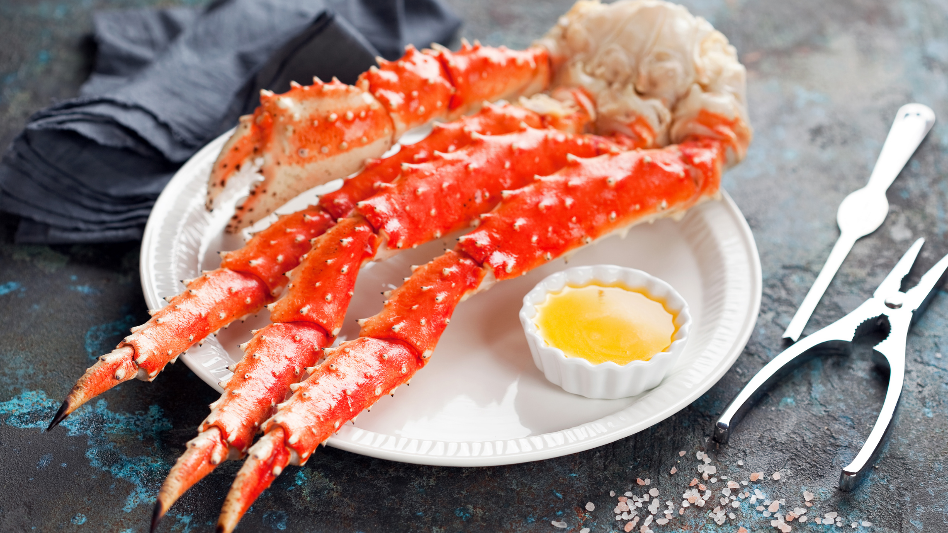 Bright red steamed king crab legs served on a white plate with a side of garlic butter and seafood cracking tools.