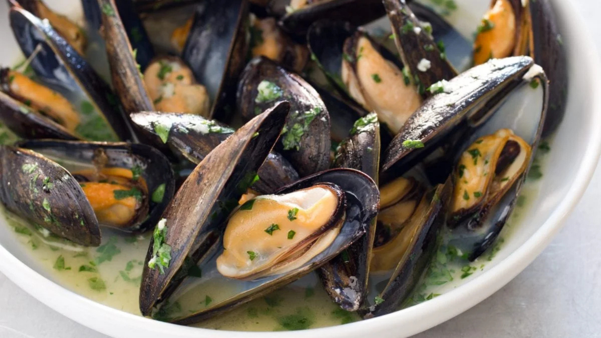 Bowl of steamed Prince Edward Island mussels in a white wine and garlic broth, garnished with chopped parsley.
